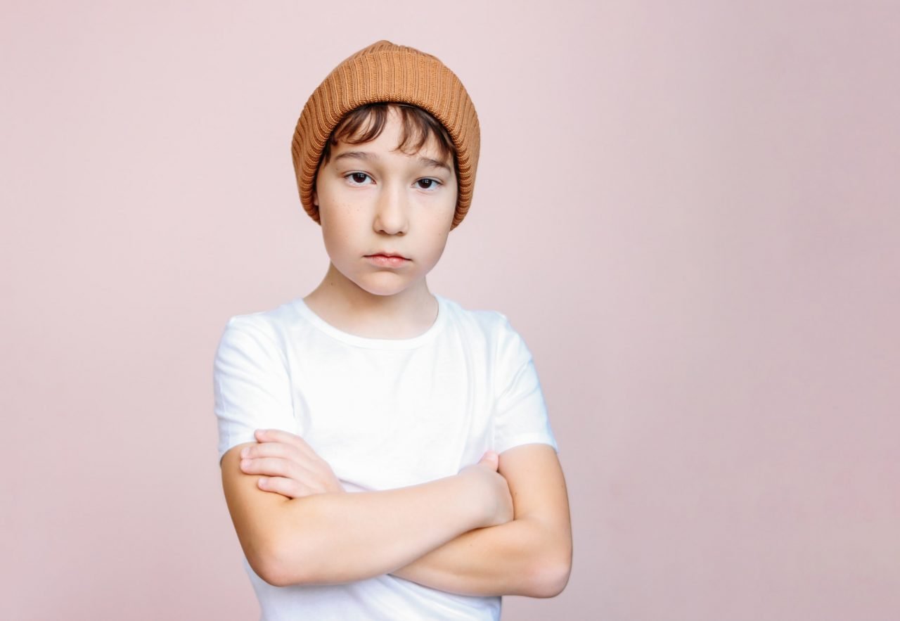 attractive-tween-boy-with-dark-hair-in-hat-looks-at-camera-on-light-pink-background.jpg